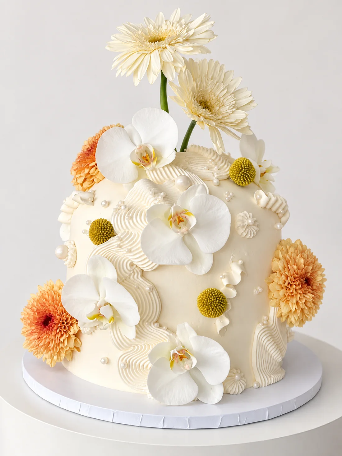 White custom cake with white orchids, peach chrysanthemums and piped wave texture