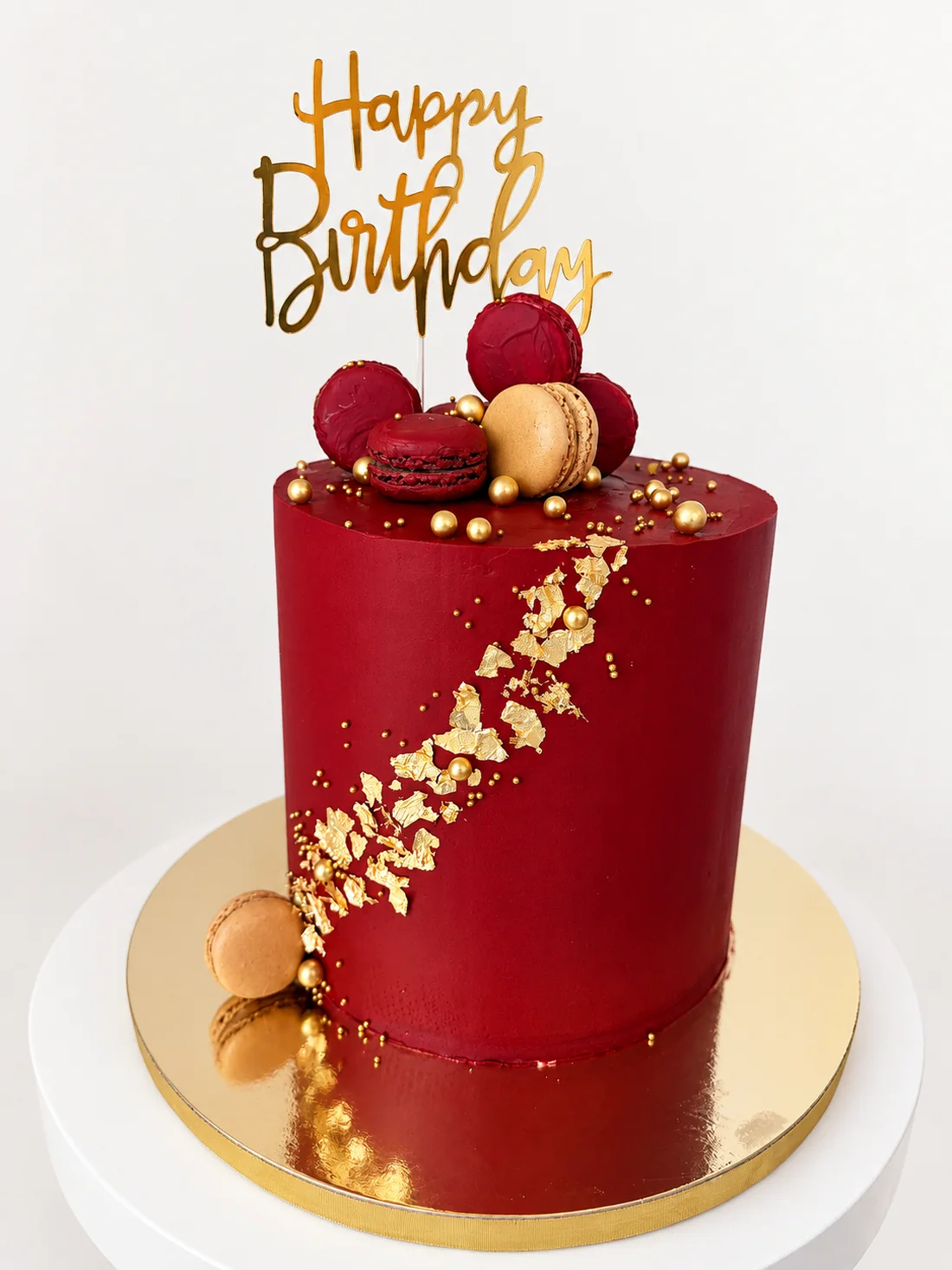 Burgundy custom cake with gold leaf, gold pearls, macarons and a Happy Birthday topper