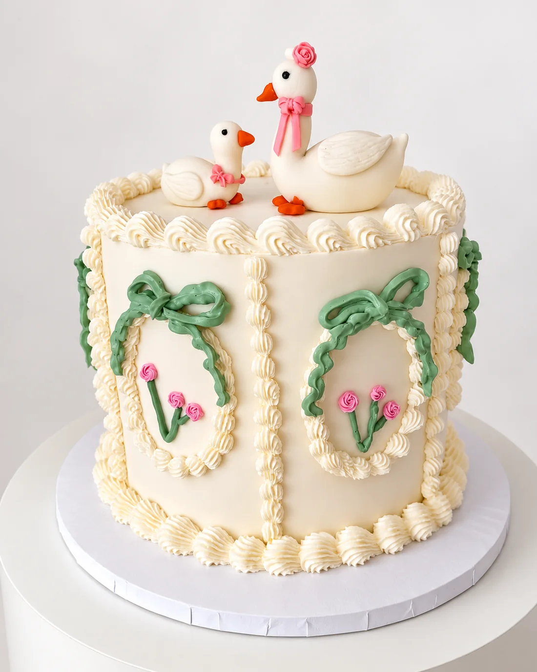 Vintage piped baby shower cake with two fondant geese, green bows and pink rosettes